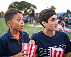 Two boys with popcorn watch outdoor movie.